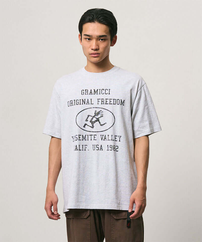 Model wearing a Gramicci ash heather colored Yosemite Valley Tee with a graphic against a light-tone background.