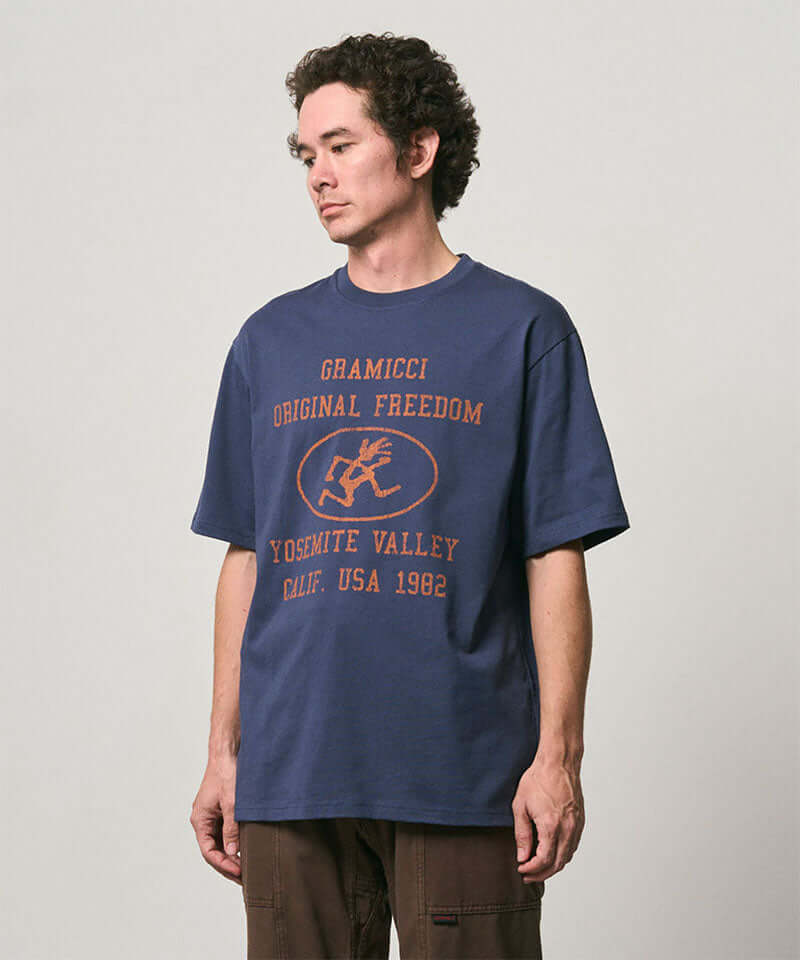 Model wearing a Gramicci navy Yosemite Valley Tee with a graphic against a light-tone background.
