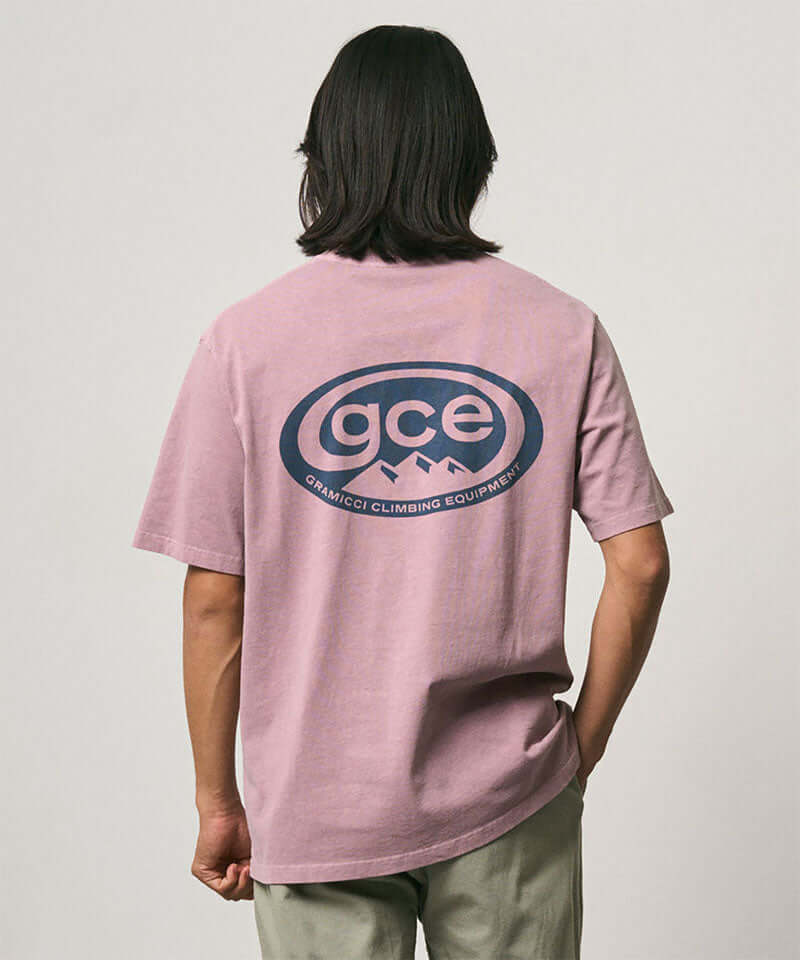 Model wearing a Gramicci lilac pigment colored GCE Tee Pigment Dyed with a graphic against a light-tone background.