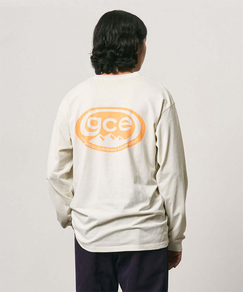 Back view of a model wearing a Gramicci natural pigment colored GCE Tee Pigment Dyed with a graphic against a light-tone background.