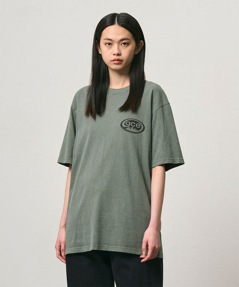 Model wearing a Gramicci sage pigment colored GCE Tee Pigment Dyed against a light-tone background.