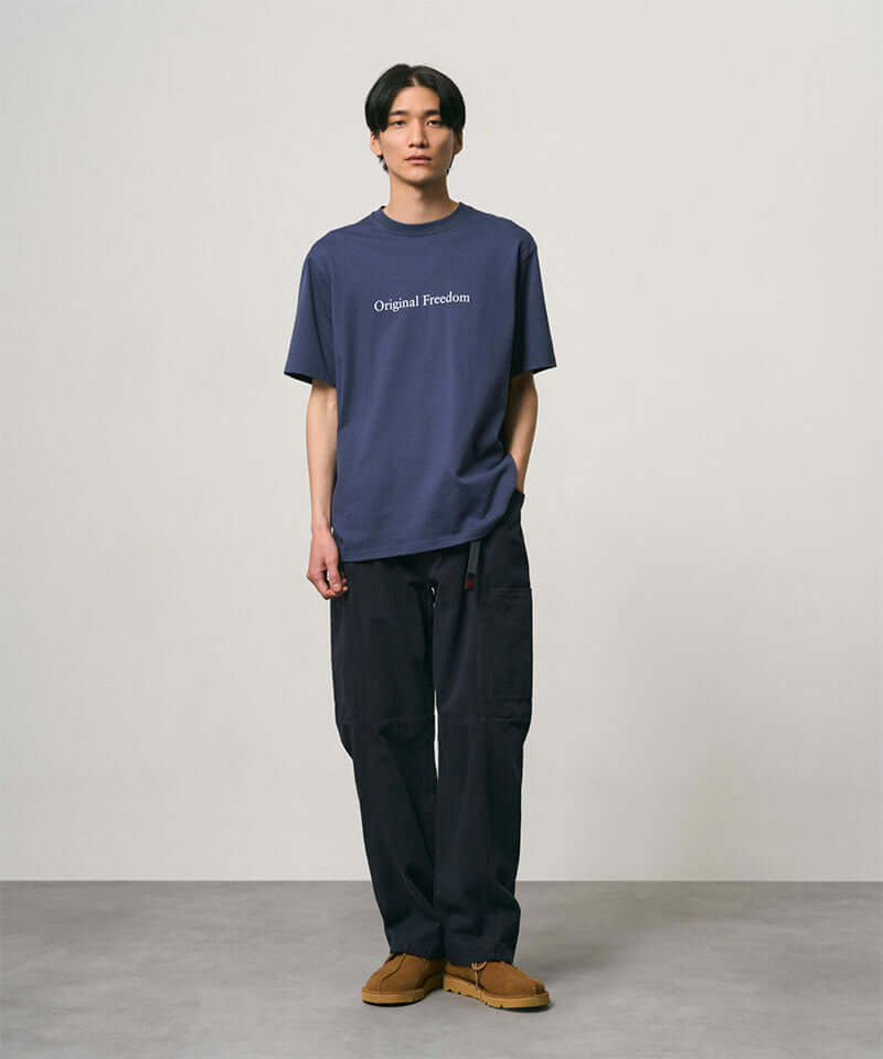 Model wearing a navy Gramicci Vase Tee and black pants on a light-tone background.