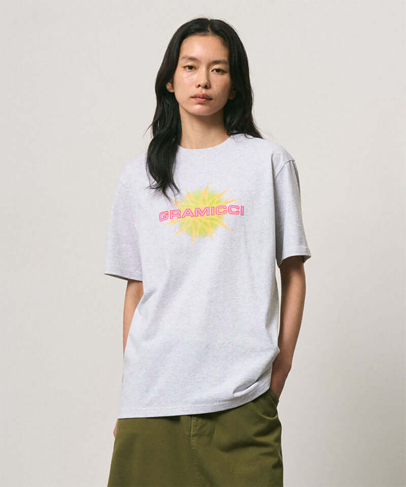 Model wearing a Gramicci ash heather colored Starburst Tee with a graphic against a light-tone background.