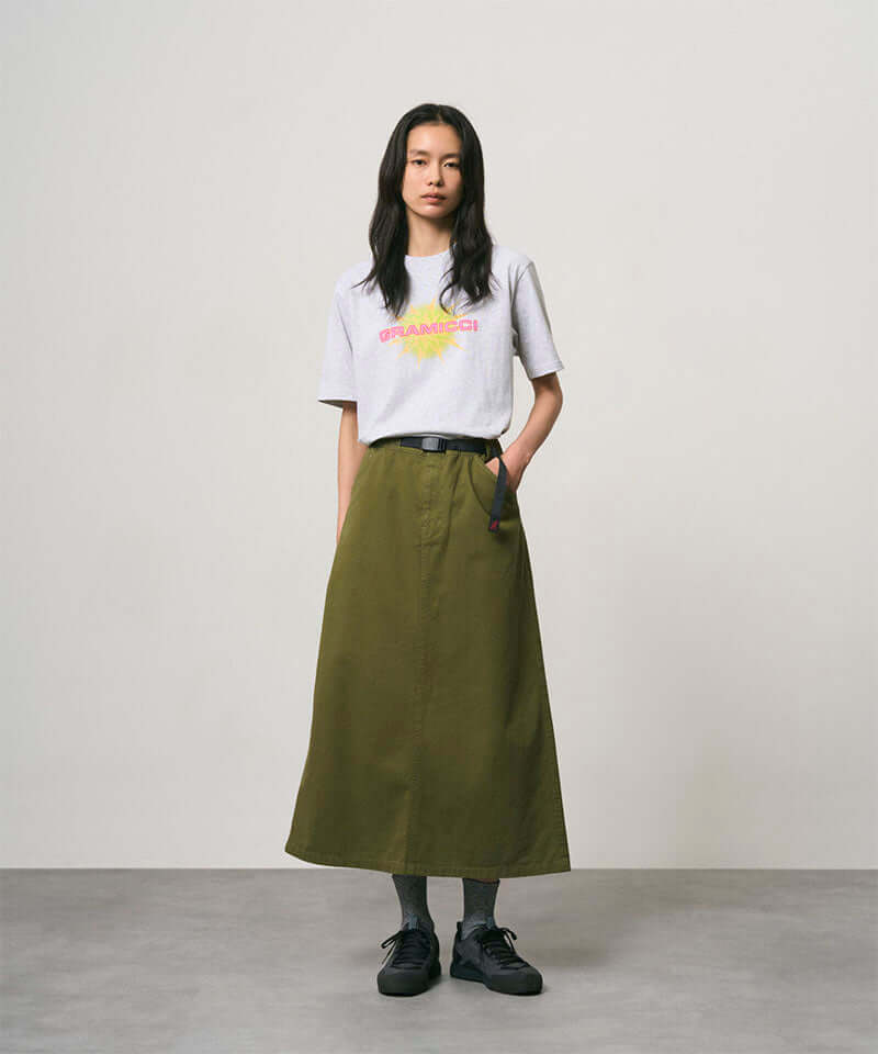 Model wearing a ash heather colored Gramicci Starburst Tee with a graphic and olive skirt on a light-tone background.