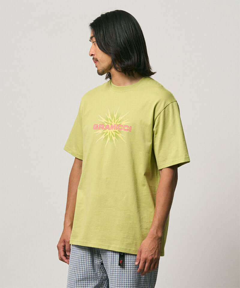 Model wearing a Gramicci sweet pea colored Starburst Tee with a graphic against a light-tone background.