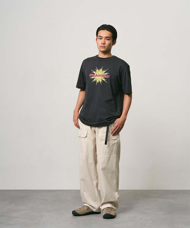 Model wearing a vintage black Gramicci Starburst Tee with a graphic and creme colored pants on a light-tone background.