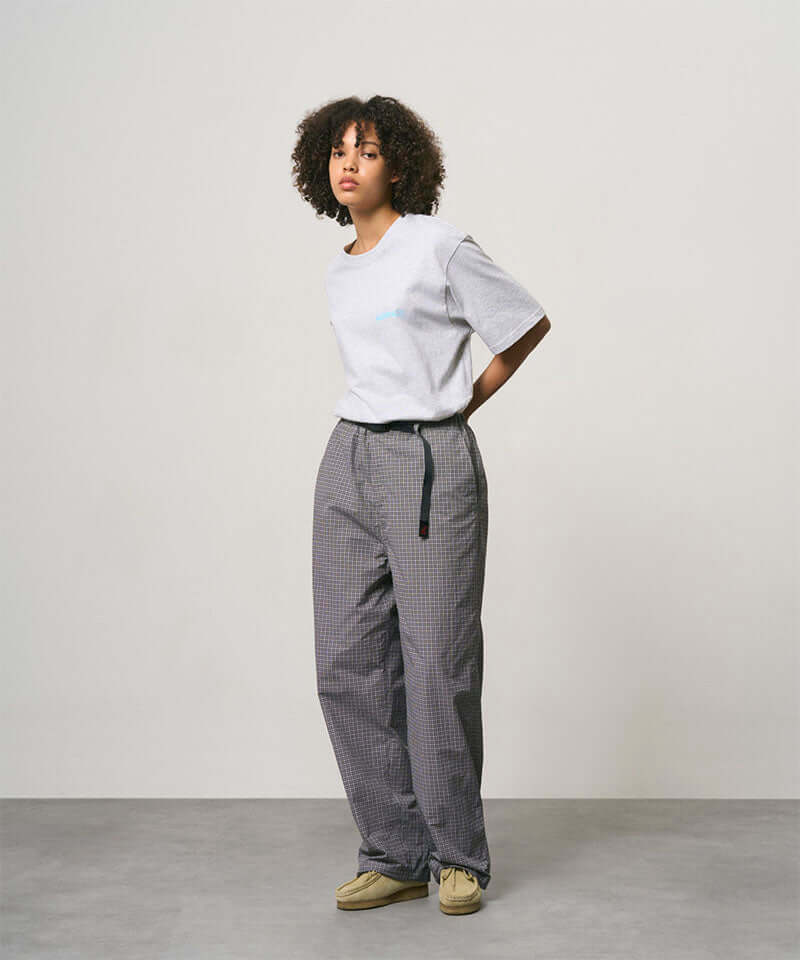 Model wearing a ash heather color Gramicci Joker Tee and grey pants on a light-tone background.
