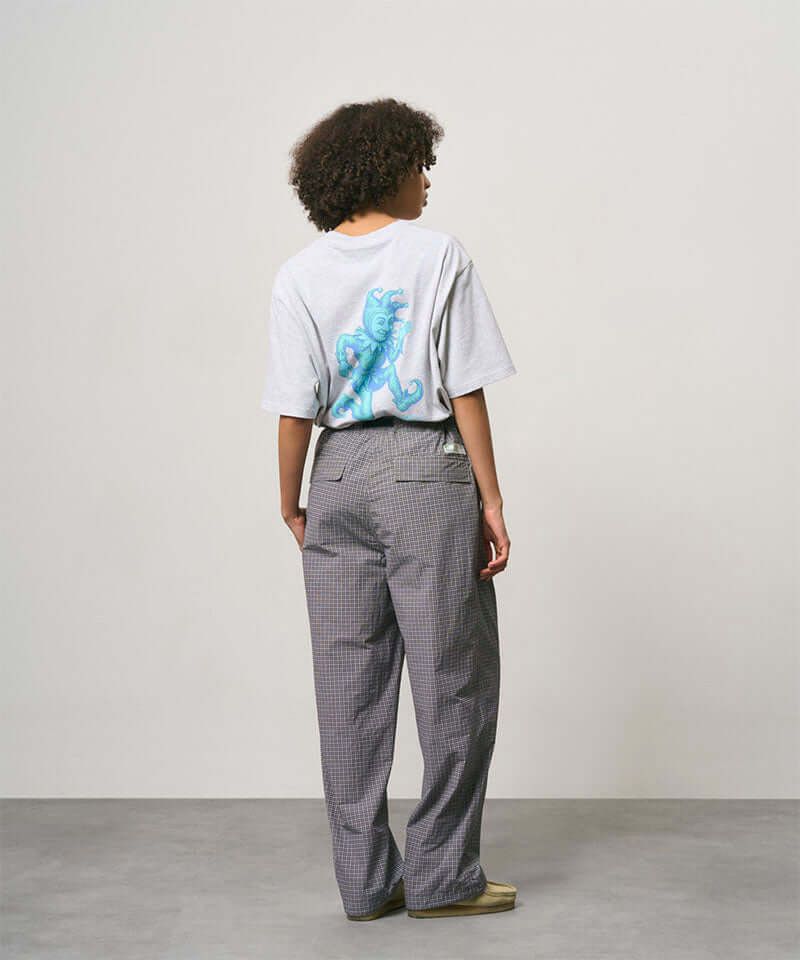 Back view of a model wearing a ash heather color Gramicci Joker Tee with a teal graphic and grey pants on a light-tone background.