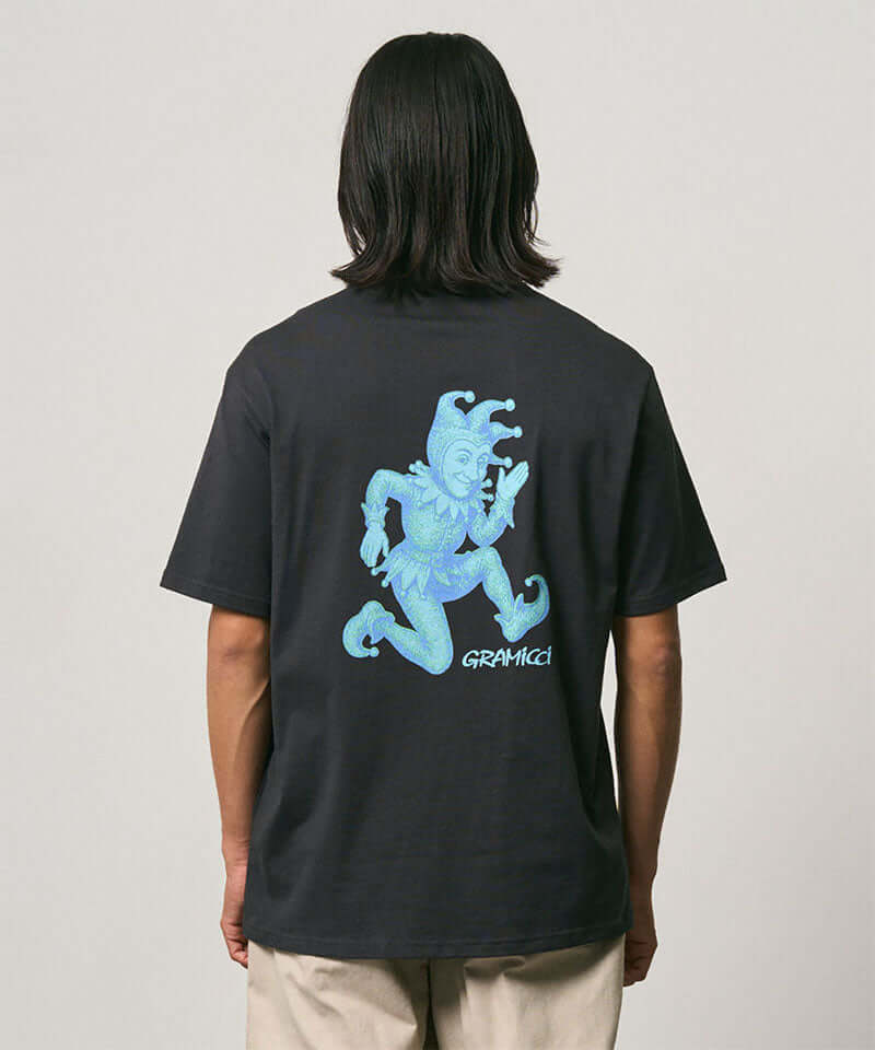 Back view of a model wearing a Gramicci vintage black Joker Tee with a teal graphic against a light-tone background.