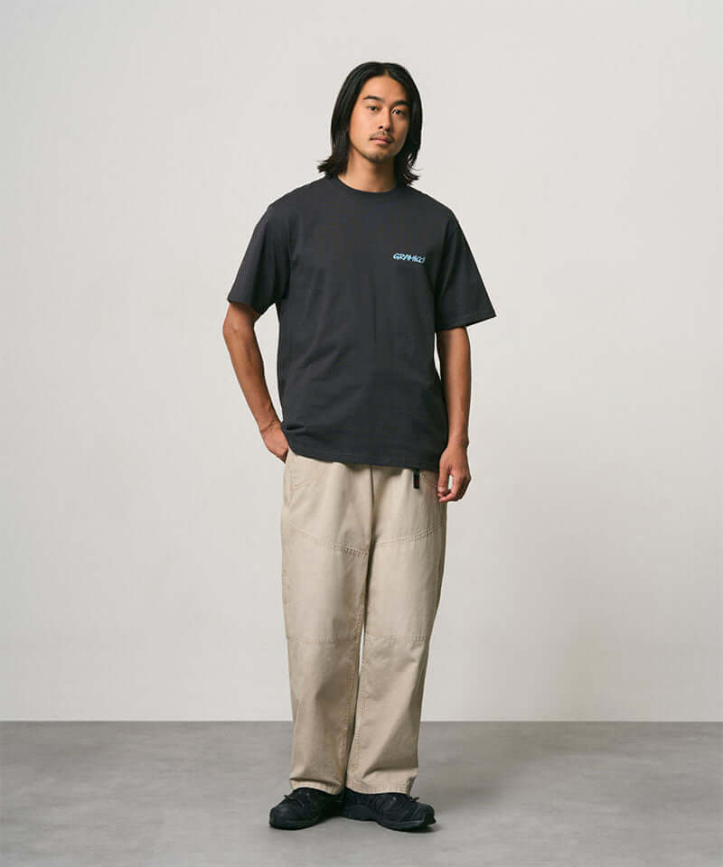 Model wearing a vintage black Gramicci Joker Tee with a teal graphic and beige pants on a light-tone background.