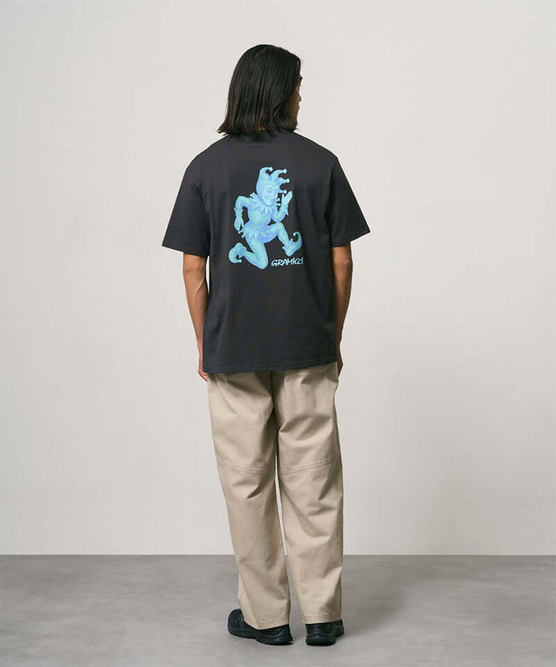 Back view of a model wearing a vintage black Gramicci Joker Tee with a teal graphic and beige pants on a light-tone background.
