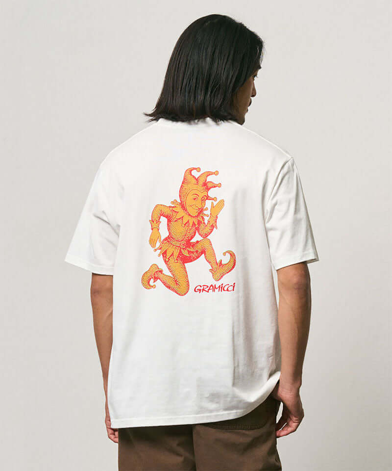 Model wearing a Gramicci white Joker Tee with an orange graphic against a light-tone background.