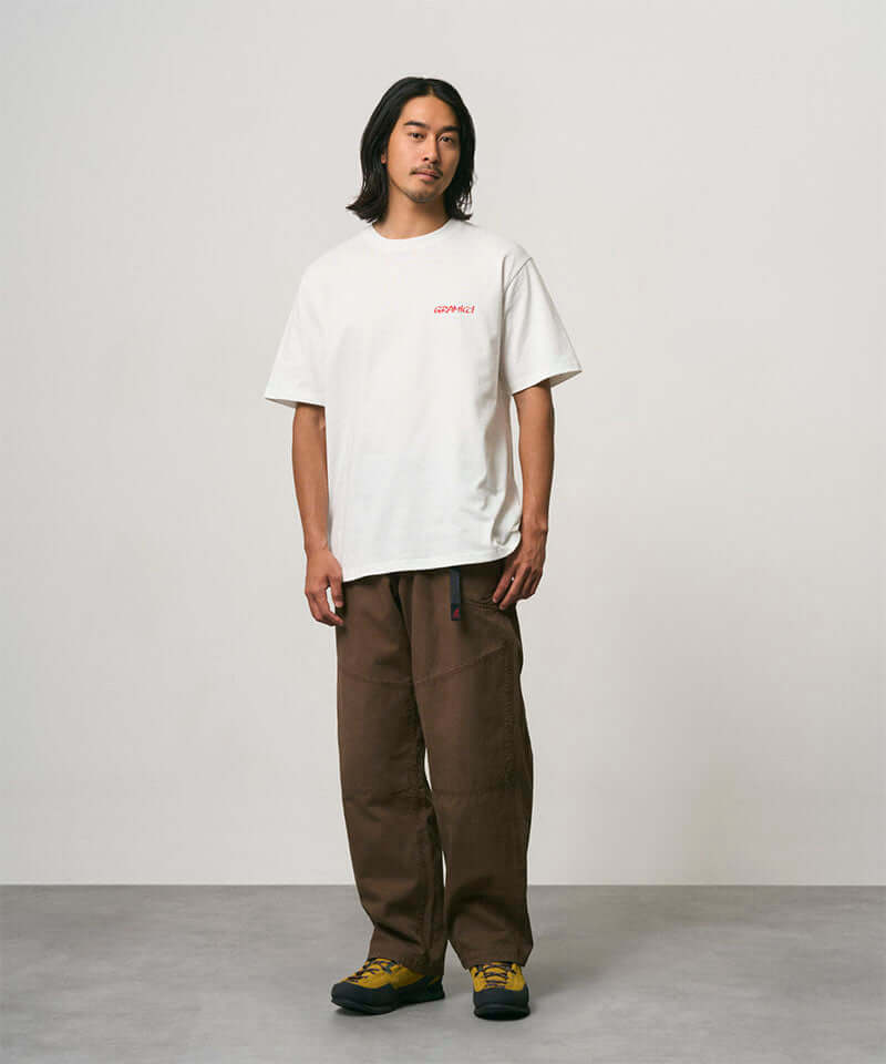 Model wearing a white Gramicci Joker Tee and light green pants on a light-tone background.