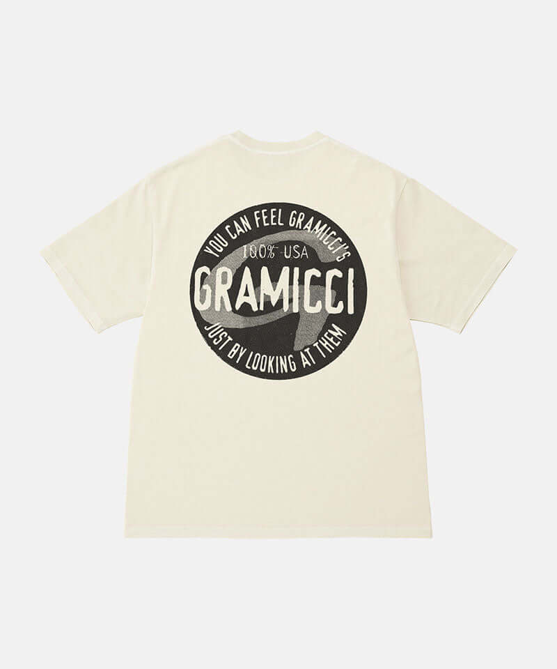 Back view of a Gramicci natural pigment colored Icon Tee Pigment Dyed with a graphic against a light-tone background.
