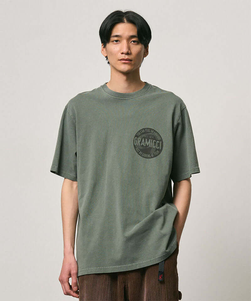 Model wearing a Gramicci sage pigment colored Icon Tee Pigment Dyed with a graphic against a light-tone background.