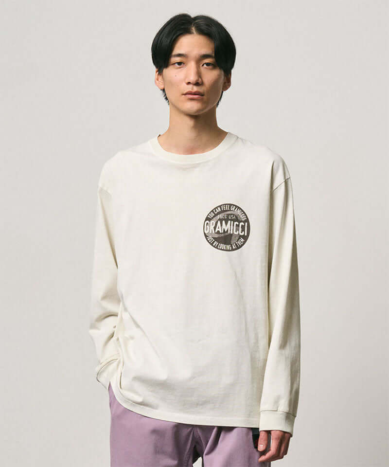 Model wearing a Gramicci natural pigment colored Icon Long Sleeve Tee Pigment Dyed with a graphic against a light-tone background.