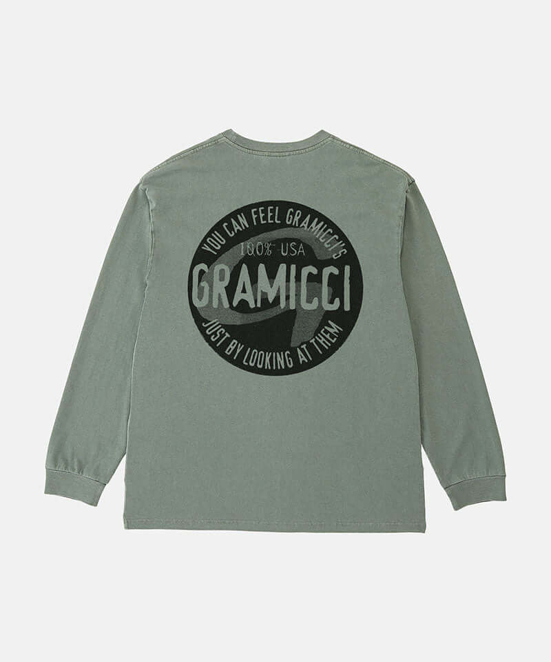 Back view of a Gramicci sage pigment colored Icon Long Sleeve Tee Pigment Dyed with a graphic against a light-tone background.