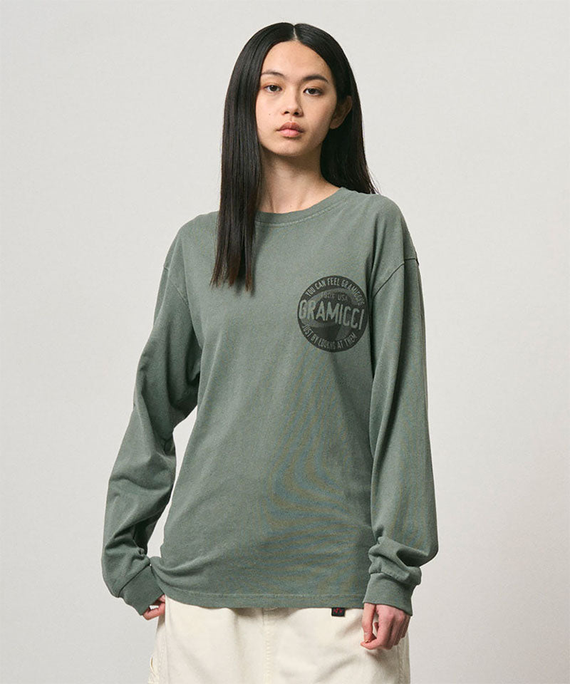 Model wearing a Gramicci sage pigment colored Icon Long Sleeve Tee Pigment Dyed with a graphic against a light-tone background.
