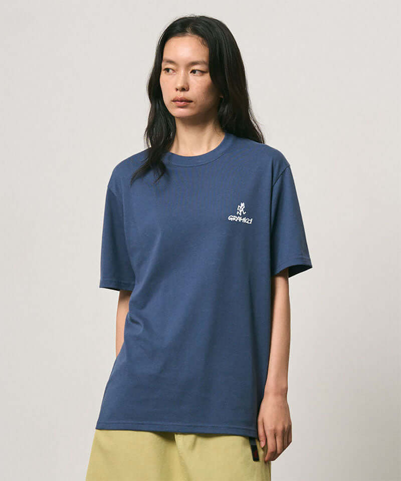 Model wearing a Gramicci dusky blue One Point Logo Tee with a graphic against a light-tone background.