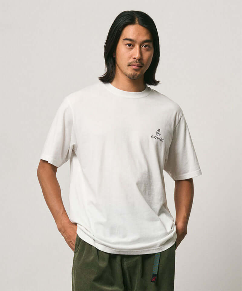 Model wearing a Gramicci white One Point Logo Tee with a graphic against a light-tone background.
