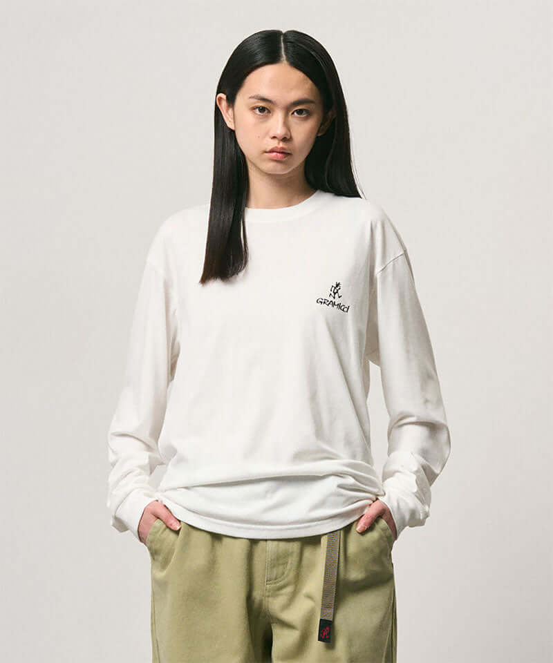 Model wearing a Gramicci white One Point Logo Long Sleeve Tee with a graphic against a light-tone background.