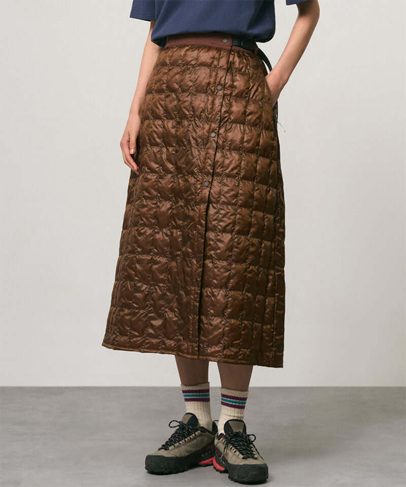 Model wearing a cola colored Gramicci G-Zero Primaloft Skirt and a blue shirt on a light-tone background.