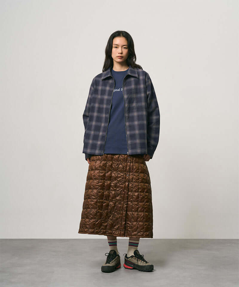 Model wearing a cola colored Gramicci G-Zero Primaloft Skirt and a blue plaid shirt on a light-tone background.