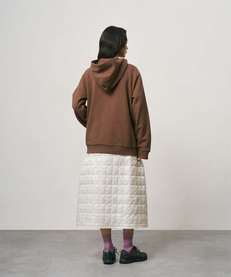 Back view of a model wearing a frost colored Gramicci G-Zero Primaloft Skirt and a brown hoodie on a light-tone background.