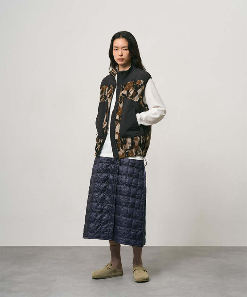 Model wearing a indigo Gramicci G-Zero Primaloft Skirt and a black and brown camo vest on a light-tone background.