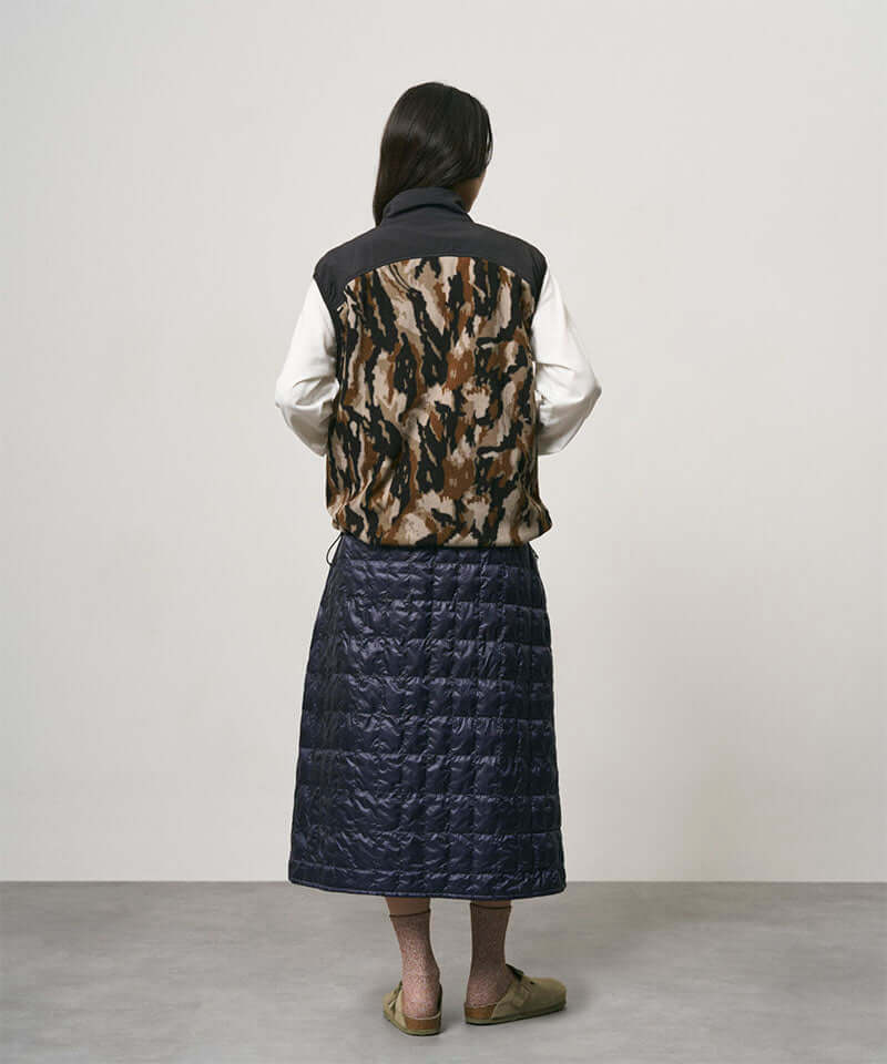 Model wearing a indigo Gramicci G-Zero Primaloft Skirt and a black and brown camo vest on a light-tone background.