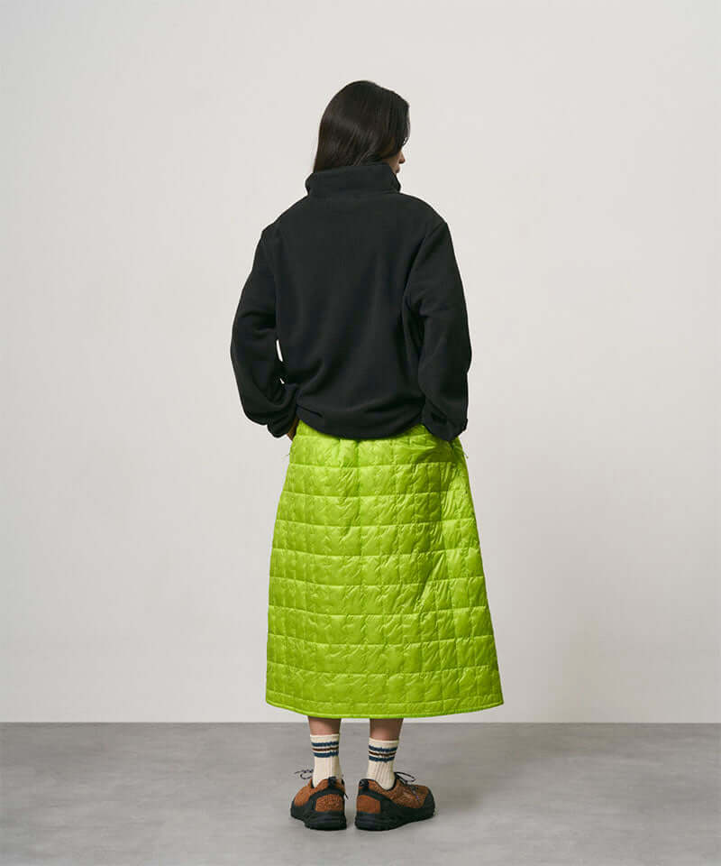 Model wearing a lime colored Gramicci G-Zero Primaloft Skirt and a black jacket on a light-tone background.