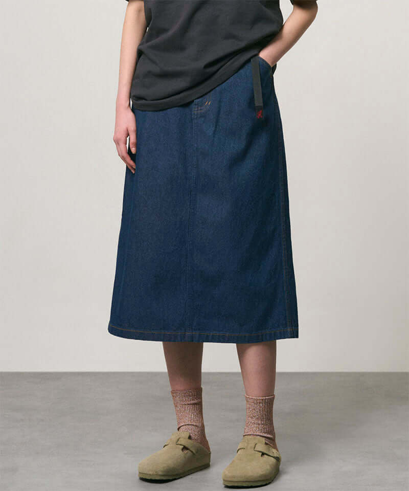 Model wearing a rinsed indigo Gramicci Denim Carpenter Skirt and a black shirt on a light-tone background.