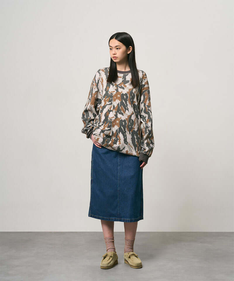 Model wearing a stone colored Gramicci Denim Carpenter Skirt and a camo sweatshirt on a light-tone background.