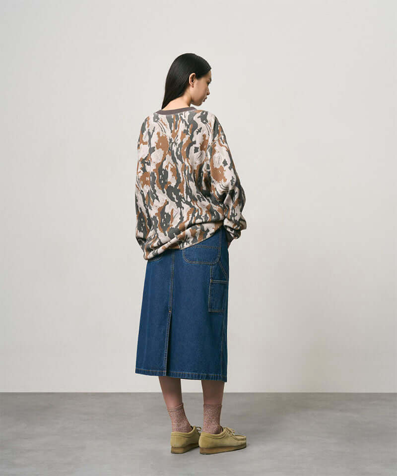 Back view of a model wearing a stone colored Gramicci Denim Carpenter Skirt and a camo sweatshirt on a light-tone background.