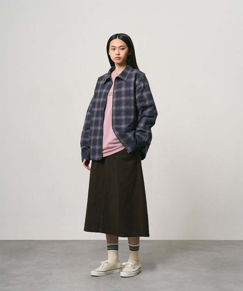 Model wearing a coffee colored Gramicci Venture Skirt and a blue plaid shirt on a light-tone background.