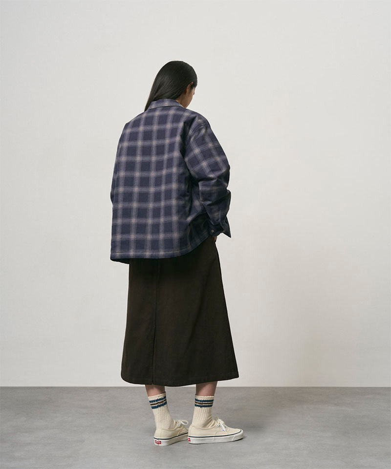Back view of a model wearing a coffee colored Gramicci Venture Skirt and a blue plaid shirt on a light-tone background.