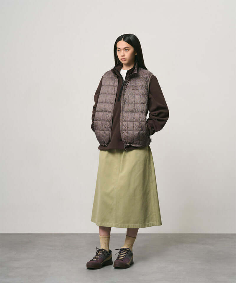 Model wearing a elm colored Gramicci Venture Skirt and a brown vest on a light-tone background.