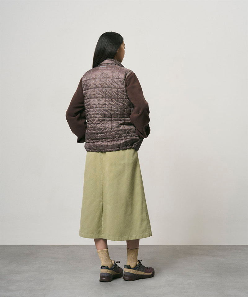 Back view of a model wearing a elm colored Gramicci Venture Skirt and a brown vest on a light-tone background.