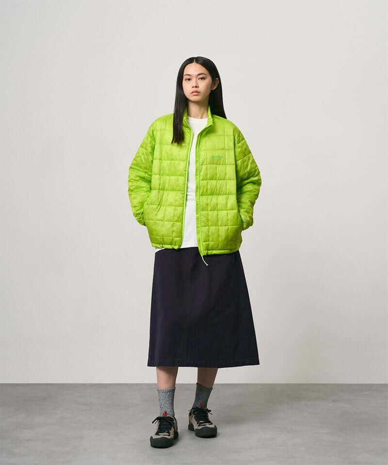 Model wearing a ink colored Gramicci Venture Skirt and a bright green jacket on a light-tone background.