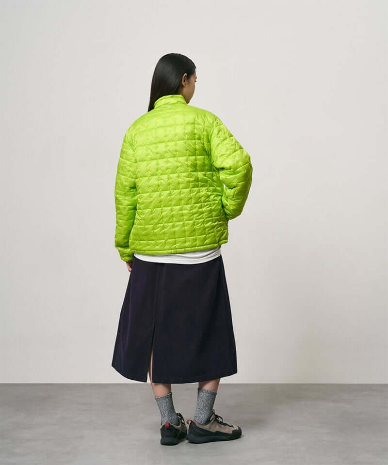 Back view of a model wearing a ink colored Gramicci Venture Skirt and a bright green jacket on a light-tone background.