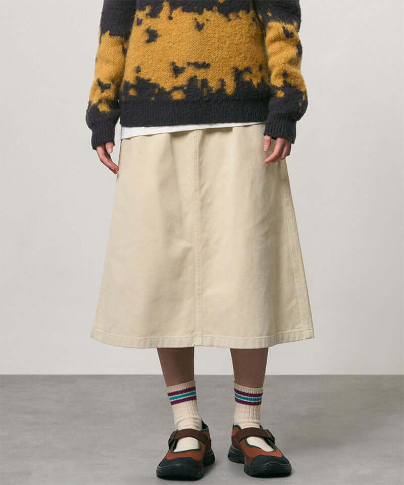 Model wearing a sand colored Gramicci Venture Skirt and a yellow and black tie-die sweater on a light-tone background.