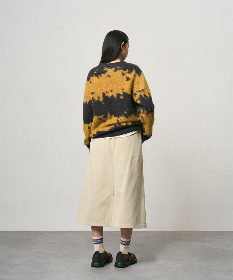 Back view of a model wearing a sand colored Gramicci Venture Skirt and a yellow and black tie-die sweater on a light-tone background.