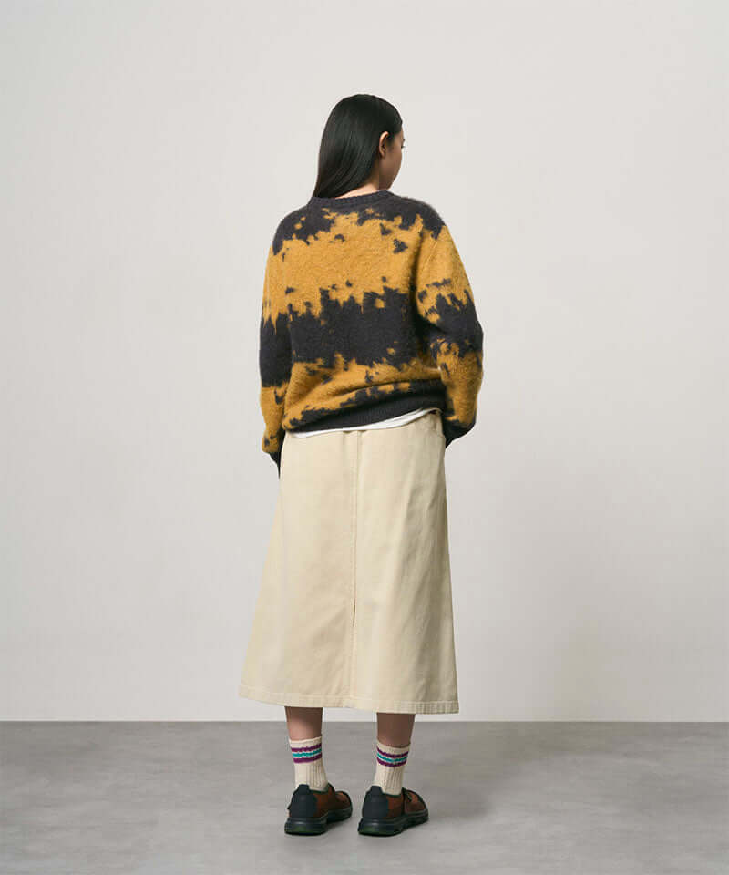 Back view of a model wearing a sand colored Gramicci Venture Skirt and a yellow and black tie-die sweater on a light-tone background.