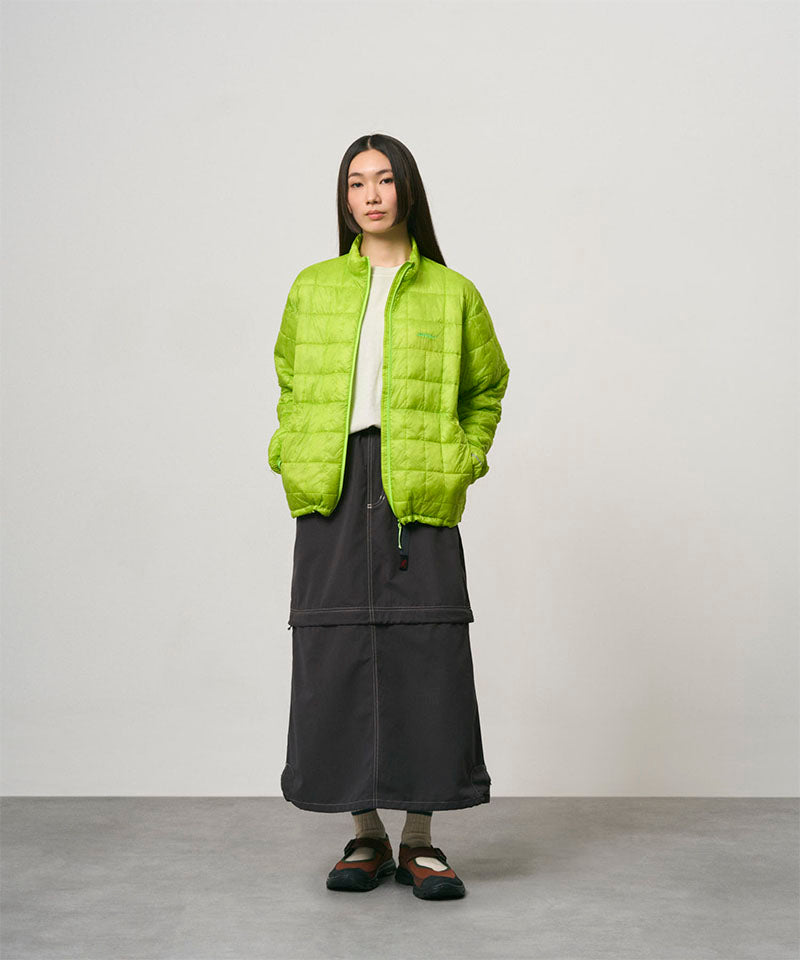 Model wearing a black women's Gramicci WR Convertible Skirt and a bright green jacket on a light-tone background.