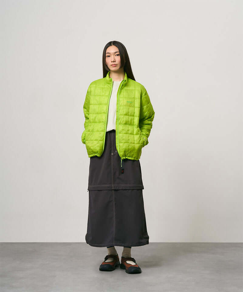 Model wearing a black women's Gramicci WR Convertible Skirt and a bright green jacket on a light-tone background.