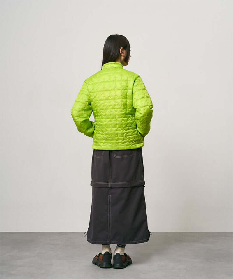Back view of a model wearing a black women's Gramicci WR Convertible Skirt and a bright green jacket on a light-tone background.