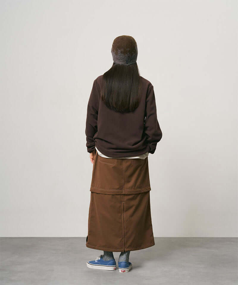 Back view of a model wearing a deep brown women's Gramicci WR Convertible Skirt and a dark brown shirt on a light-tone background.
