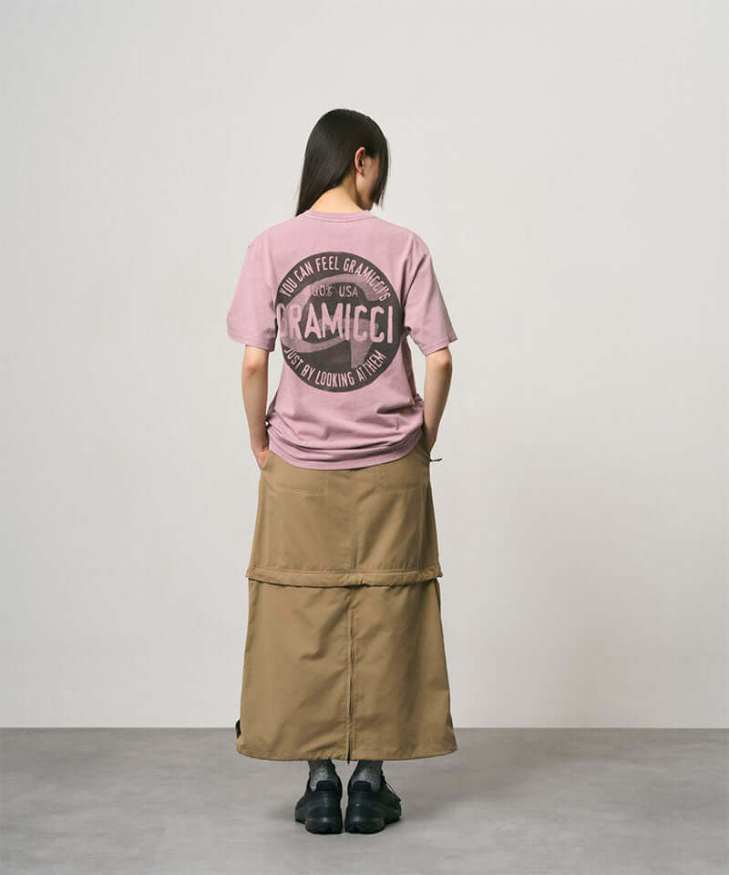 Back view of a model wearing a khaki colored women's Gramicci WR Convertible Skirt and a dusty pink shirt on a light-tone background.