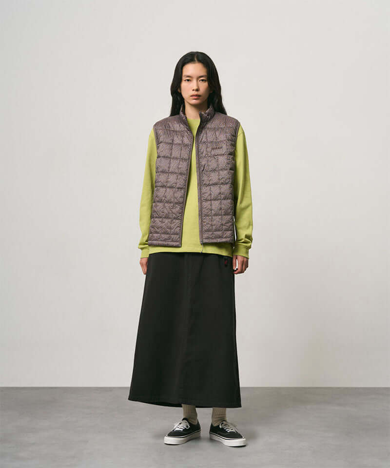 Model wearing a black Gramicci 5-Pocket Skirt and a brown vest on a light-tone background.