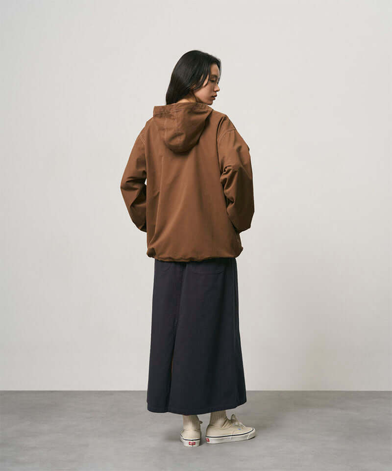 Back view of a model wearing a double navy Gramicci 5-Pocket Skirt and a brown jacket on a light-tone background.